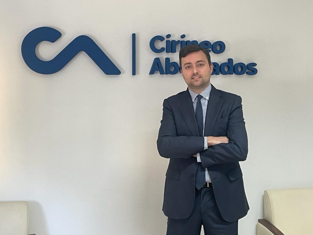 Hombre en traje posando frente al logo de Cirineo Abogados.