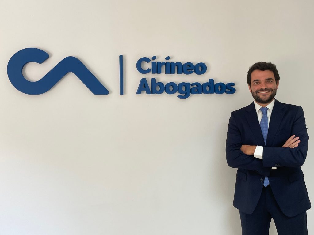 Hombre en traje sonriendo frente al logo de Cirineo Abogados.