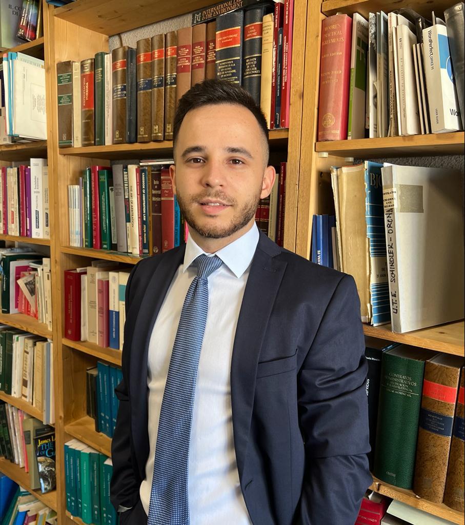 Abogado joven en traje frente a una estantería de libros.