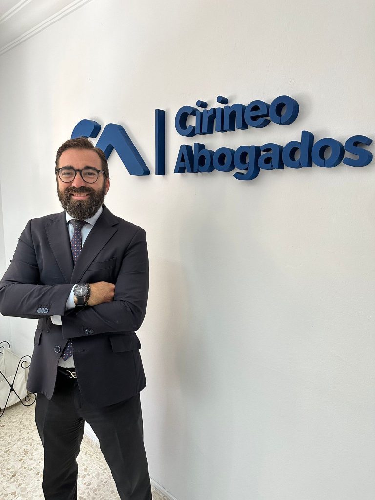 Hombre con barba y traje posando junto al logo de Cirineo Abogados.