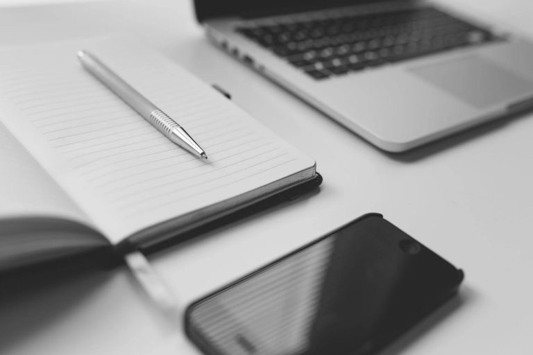 Cuaderno, bolígrafo y laptop en una mesa de trabajo.